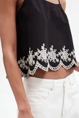 Top negro de algodón con breteles finos que se atan en moño y detalle de bordado floral blanco en el ruedo.
