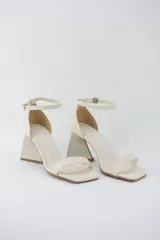 Sandalias color crema con tira delgada sobre los dedos, pulsera al tobillo con hebilla y taco geométrico.