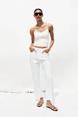 Jeans tobilleros de tiro alto color blanco, corte recto y bajo sin costura. Cierre frontal cruzado con cremallera y botones.
