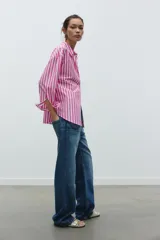 Camisa de popelín a rayas verticales rosas y blancas, de corte holgado, con cuello solapa, escote pico y mangas largas con puños abotonados.