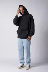 Buzo canguro negro con capucha, calce oversize, confeccionado en frisa 100% algodón con lavado gastado y aplique cosido en el pecho.