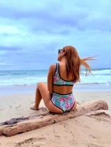 Conjunto de bikini estampado con flores y hojas en tonos celeste, turquesa, rosa y violeta. El corpiño es deportivo con breteles negros y la bombacha es de tiro alto con ribete negro.