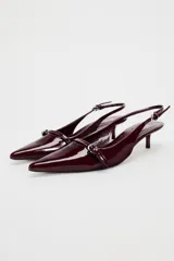 Zapato destalonado color borgoña charol, con tacón kitten y punta fina. Presenta una tira trasera con hebilla ajustable y detalle de hebilla metálica en la parte delantera.