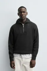 Jersey de punto perlado negro, de corte relaxed fit, con cuello perkins y cierre frontal de cremallera.
