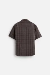 Camisa de hombre color gris con diseño a cuadros, corte relaxed fit, cuello bowling, manga corta y cierre frontal con botones.
