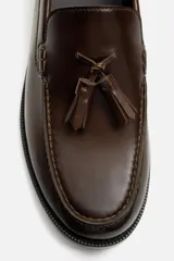 Mocasín de vestir color marrón oscuro, con detalle de borlas en la parte delantera.
