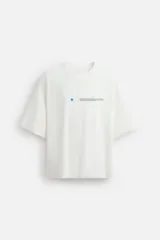 Camiseta blanca de corte holgado, cuello redondo y manga corta. Presenta un pequeño estampado de una estrella azul y un texto en negro en el frente.
