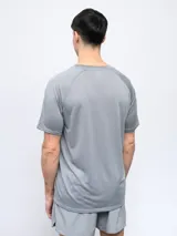 Remera deportiva Umbro color gris claro con patrón de rayas horizontales sutiles en el cuerpo y paneles lisos en hombros y mangas. Posee cuello redondo y logo Umbro en rojo en el pecho.