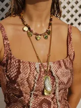 Collar de doble cadena dorada. La cadena superior es de piedras irregulares marrones, amarillas y naranjas con dijes circulares dorados. La cadena inferior es de eslabones dorados con un dije rectangular dorado y plateado.