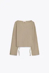 Top mostaza de cuello barco y manga larga con textura. Tiene lazadas ajustables en el bajo.