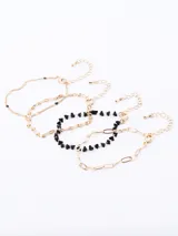 Set de tres pulseras doradas, una de eslabones grandes, otra de eslabones pequeños y una con piedras negras irregulares.