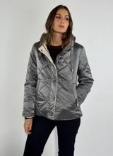 Campera plateada con capucha, cierre frontal con botones a presión y diseño acolchado con patrón de rombos.