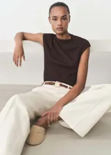 Camiseta color beige de tejido fluido con cuello asimétrico, diseño recto y detalles fruncidos.