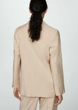 Blazer color beige con rayas verticales finas, cuello con solapa de muesca, corte recto, cierre frontal con botón, dos bolsillos con solapa y mangas largas con puños abotonados.
