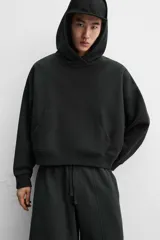 Sudadera negra corta con capucha, manga larga, bolsillo tipo canguro y terminaciones en rib.