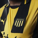 Camiseta de fútbol Puma del Club Atlético Peñarol, modelo Home 2025. Diseño a rayas verticales amarillas y negras con detalles en negro en cuello y mangas. Incluye logo de Puma, escudo del club y sponsor Antel en el frente.