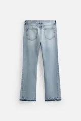 Pantalón de jean negro con efecto lavado, corte flare, cinco bolsillos, cierre frontal con cremallera y botón, y bajo con acabado irregular.