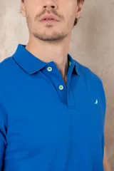 Chomba azul con cuello clásico, tapeta de dos botones y logo bordado en el pecho.