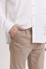 Pantalón de vestir color beige, de corte recto, con pinzas en la cintura, bolsillos laterales y traseros. Se ajusta a la cintura con cinturón de cuero marrón.