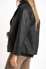 Chaqueta tipo gamulán de color negro con forro de corderito sintético al tono. Presenta solapas anchas, cierre frontal con botones y un diseño entallado al cuerpo.