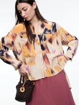 Camisa de manga larga confeccionada en viscosa crinkled con estampa de manchas en tonos beige, amarillo, naranja, negro y violeta. De silueta amplia y fluida, con cuello camisero, cierre frontal con botones, bolsillos frontales grandes, tajos laterales y largo extendido en la espalda.