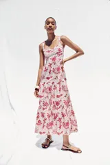 Vestido midi con estampado floral en tonos rosados, de escote recto y tirantes anchos con abalorios. Presenta aberturas laterales en la cintura y cierre trasero con cremallera oculta.