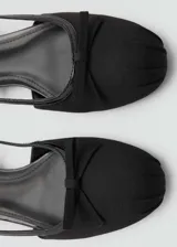 Zapato tipo ballerina color negro, con efecto piel, punta redonda, lazo decorativo y cierre de tira con hebilla.