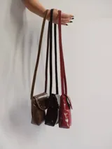 Bandolera porta celular marrón de cuero con solapa y cierre con botón a presión. Presenta tachas metálicas plateadas en el borde de la solapa y correa fina para colgar al hombro.