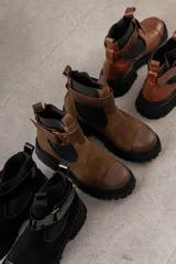 Botas de cuero color marrón oscuro, estilo Chelsea, con elástico lateral negro y suela track negra. Incluye correa de cuero desmontable con hebilla.