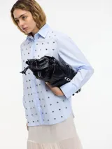 Camisa blanca de algodón con cuello camisero, cierre frontal con botones y tachas plateadas en el frente.