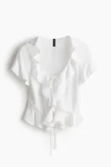 Blusa blanca entallada corta en tejido liviano de mezcla de lino y viscosa. Modelo de manga corta con escote redondo pronunciado, delantero abierto con tira fina doble y cordón para ajustar en la cintura. Volados anchos en escote, abertura, mangas y bajo.