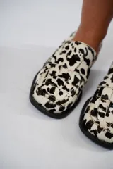 Mocasín de cuero con estampado animal print de vaca en tonos marrón y blanco, con capellada enrejillada y suela plana con plataforma delantera y taco bajo.