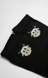 Medias negras de caña media con diseño de vaca bordado en la parte superior y logo de la marca con tijeras en la planta del pie.