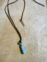 Collar con cordón de cuero marrón, dije de piedra color miel y detalle de cristal plateado.