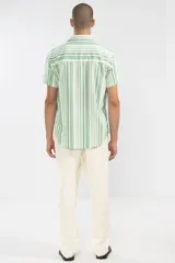 Camisa de manga corta con rayas verticales en tonos verde, blanco y gris. Tiene cuello clásico, bolsillo en el pecho y botones de coco.