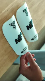 Espinilleras blancas con logo de la marca en negro.