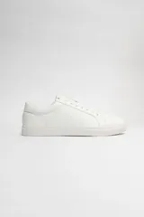 Zapatillas acordonadas blancas de cuero sintético, con suela plana de goma y cordones blancos.
