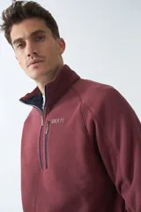 Buzo polar de algodón color bordó, con cuello elevado, medio cierre frontal, bolsillo con cierre en el pecho y logo estampado.
