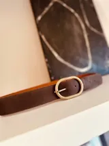 Cinturón marrón de cuero con hebilla ovalada dorada.