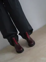 Botas de cuero color borgoña con suela track y cremallera frontal roja.