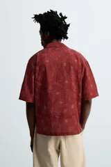Camisa color ladrillo con estampado de flores en relieve, corte relaxed fit, cuello bowling, manga corta, bajo con aberturas laterales y cierre frontal con botones.