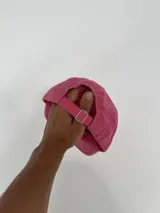 Gorro tipo gorra color fucsia con visera, y estampado frontal en azul con la palabra "attitude" y otros textos.