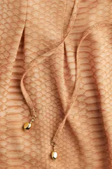 Blusa de gasa color ocre con estampado de piel de serpiente, escote en V pronunciado con tiras diagonales y mangas extralargas acampanadas.