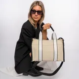 Bolso tipo tote color beige con laterales negros, doble asa corta de mano con detalles en cuero sintético negro y correa larga de hombro negra regulable y extraíble.