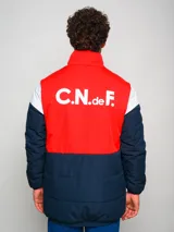 Campera parka de hombre con cuello alto, cierre frontal con cremallera y broches a presión, y escudo del Club Nacional de Football en el pecho. Diseño a bloques de color azul marino, blanco y rojo.