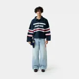 Polo de manga larga color azul marino, con cuello clásico y cierre de botones. Presenta rayas horizontales blancas y bordó en el pecho y las mangas, y el logo "EMESTUDIOS" estampado en blanco en el frente. Tiene un corte holgado.