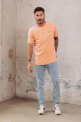 Remera color durazno de corte recto y manga corta, con cuello redondo y pequeño bordado de dos patos en el pecho.