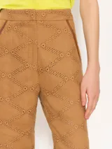 Pantalón flare color camel de broderie con aberturas en botamangas cerradas con broches dorados. Presenta bolsillos delanteros diagonales con vivos en cuero al tono.