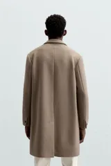 Abrigo straight fit color beige confeccionado en tejido con lana. Cuello con solapas de muesca, manga larga acabada en puño con botones, bolsillos de vivo en cadera, detalle de bolsillo interior y bajo con abertura en centro espalda. Cierre frontal de botonadura.
