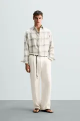 Pantalón color crema de lino, corte relaxed fit, con pliegues frontales, bolsillos laterales y traseros de vivo.